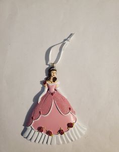 a pink princess ornament hanging from a white string on a white table top