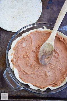 there is a pie with chocolate frosting in the pan and a wooden spoon on top