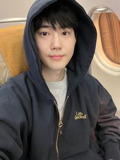 a young man sitting on an airplane seat wearing a hoodie