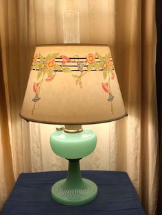 a green lamp sitting on top of a blue table next to a curtained window