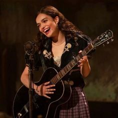 a woman holding a guitar and singing into a microphone