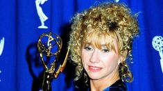 a woman with curly hair holding an award in her hand and posing for the camera