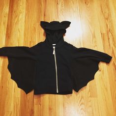 a black hooded jacket with a zipper on the front and back, sitting on a wooden floor