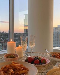 two plates of food on a table in front of a window with candles and wine glasses