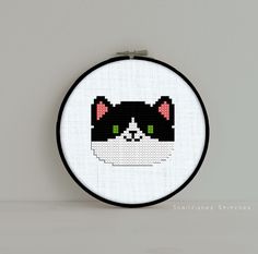 a black and white cat with green eyes cross stitched into a hoop hanging on a wall