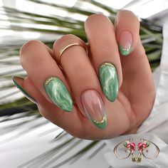 a woman's hand with green and pink nail polishes on it, next to some flowers