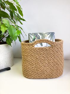 a woven basket sitting next to a potted plant on a white table with a card in it