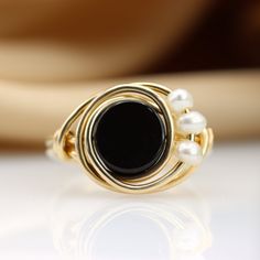 The perfect combination between Black and White This unique wire ring is set with a genuine Black onyx and three Fresh water pearls ☆ WHY THIS PIECE OF J E W E L R Y IS AWESOME! ☆ * Hand finished and made from high quality raw materials * Long lasting beauty & Timeless design ♡ WRAPPING ♡ * All 23 Summers jewels arrive in a cute pouch or gift box so they are gift ready. DELIVERY ✉ * Most items are ready made but some are made to order, Times for each items are shown on * Well packaged for do Elegant Adjustable Onyx Rings, Adjustable Onyx Rings With Black Enamel, Adjustable Black Enamel Onyx Rings, Elegant Onyx Wire Wrapped Jewelry, Elegant Handmade Black Crystal Ring, Elegant Black Pearl Ring For Gift, Elegant Wire Wrapped Round Rings, Black Hand Wrapped Round Jewelry, Black And White Ring