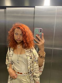 a woman with red hair taking a selfie in front of an elevator door while wearing headphones