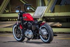 a red motorcycle parked on top of a parking lot next to a metal bridge overpass