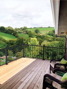 an outdoor deck with chairs and tables overlooking the green hills in the distance on a cloudy day