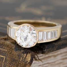 A charming throwback from the 70s, this ring showcases a central old European cut diamond that is much older than its current home, yet, flanked by these dramatic baguettes on the shoulders, it feels right at home! How set, sleek and minimalist in its overall vibe - so very very French! The OEC is incredibly bright and truly much much whiter facing than its graded color - she is a sparkle bomb, and very fiery! The baguettes all add to that vintage feel of the ring - sheer perfection! 18kt yellow Vintage Diamond Ring With Baguette Cut, Vintage Diamond Ring With Baguette Cut Center Stone, Timeless Diamond Ring With Baguette Cut And Bezel Setting, Timeless Diamond Ring With Baguette Diamonds, Timeless Baguette Cut Diamond Ring With Bezel Setting, Timeless Baguette Cut Diamond Ring, Vintage Channel Set Diamond Ring, Classic Baguette Cut Diamond Ring With Rose Cut Diamonds, Classic Baguette Cut Diamond Ring With Rose Cut