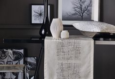 a table with two vases on it next to a white pillow and black framed pictures