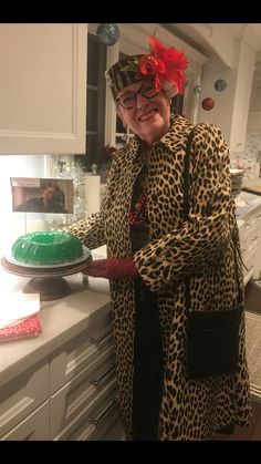 an older woman in leopard print coat holding a green cake on top of a counter