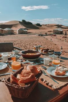 a table set with food and drinks on the beach in front of some sand dunes