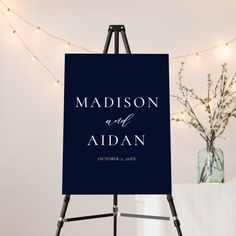 an easel with a sign that says madison and aidan on it in front of string lights