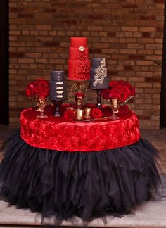 a table topped with red and black cakes on top of a cake plate covered in tulle