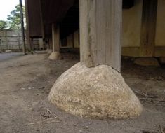 a large rock sitting on the side of a road next to a wooden pole and building