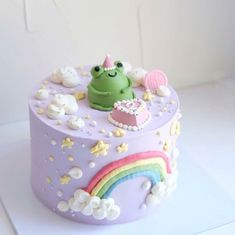 there is a cake with a frog on it and rainbows in the sky around it