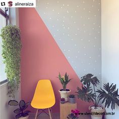 a room with some plants and a yellow chair in front of a wall painted pink and blue