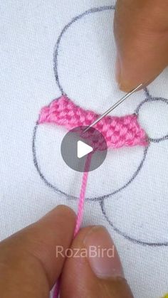 someone crocheting a mickey mouse head on a piece of white fabric with pink yarn