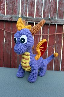 a purple crocheted dragon sitting on top of a table next to a fence