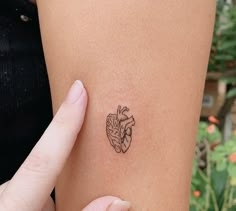 a woman holding her arm with a small tattoo on it's left side, showing the outline of a human heart