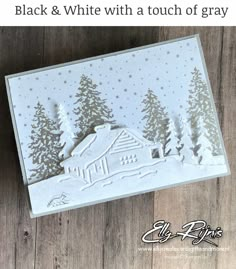 a christmas card with a house in the snow and pine trees, on a wooden surface