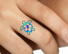 a close up of a person's hand with a tattoo on their finger and turtle ring