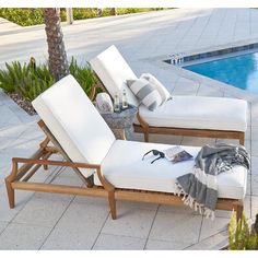 a white chaise lounge chair next to a swimming pool with sunglasses and a blanket on it