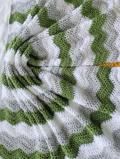 a green and white crocheted blanket laying on top of a bed next to an orange object