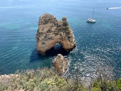 a rock formation in the ocean with a boat sailing by