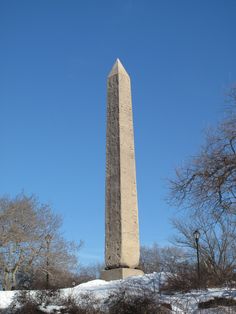 a tall obelisk in the middle of a snow covered field with trees and bushes