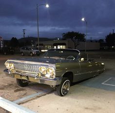 an old car is parked in a parking lot at night with the lights turned on