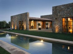 a house that is next to a pool with lights on the windows and grass in front of it