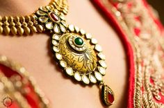 a close up shot of a woman's chest wearing an elaborate gold and green necklace