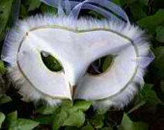 an owl mask with white feathers and blue ribbon hanging from it's side in the grass