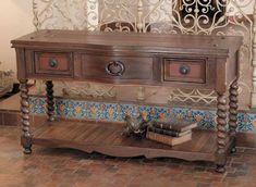 an old wooden table with two drawers and a book on the top, in front of a decorative wall