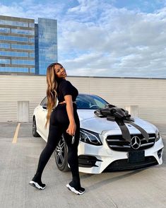 a woman standing next to a white car with a black bow on it's hood