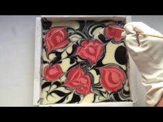 a person in white gloves holding a piece of art with red and black swirls on it