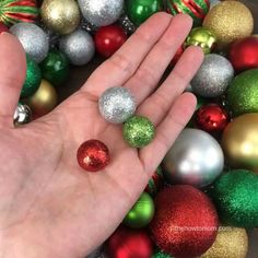 someone is holding their hand out in front of christmas balls and other holiday ornament