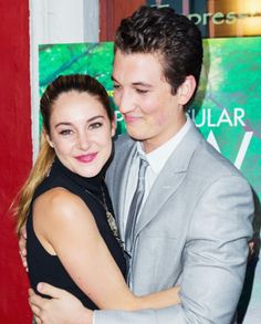 a young man and woman hugging each other in front of a red wall at an event