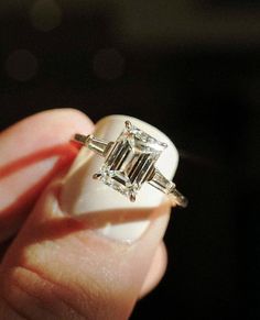 a woman's hand holding an engagement ring with three baguettes on it