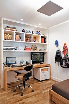 a room with a bed, desk and computer on top of wooden flooring next to a white wall