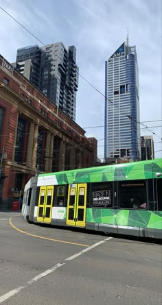 a green and yellow bus driving down a street next to tall buildings in the city