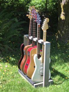 three guitars are stacked on top of each other in the grass near trees and flowers