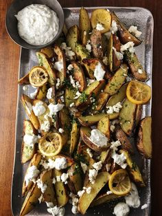 potato wedges with feta cheese and lemon slices on a platter next to a bowl of ranch dressing