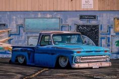 an old blue pickup truck parked in front of a building with graffiti on the walls