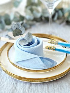 two blue napkins are sitting on a plate with gold rimmed plates and silverware