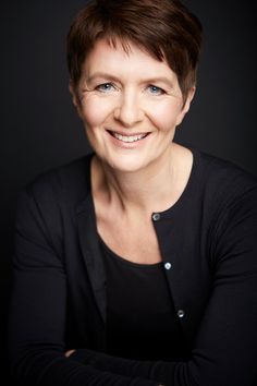 a woman with short brown hair smiling at the camera and wearing a black cardigan